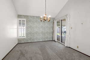 Carpeted empty room featuring vaulted ceiling and a chandelier