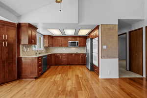 Kitchen with appliances with stainless steel finishes, light wood-style flooring, light countertops, vaulted ceiling, and decorative backsplash