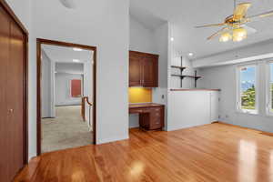 Unfurnished living room featuring built in desk, a textured ceiling, a ceiling fan, light wood-style floors, and high vaulted ceiling