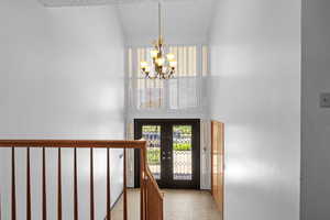 Foyer entrance featuring a chandelier, french doors, plenty of natural light, and high vaulted ceiling