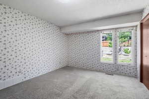Carpeted spare room with wallpapered walls and a textured ceiling