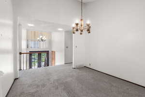 Empty room featuring a chandelier, carpet, and a high ceiling