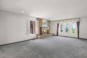 Unfurnished living room with a textured ceiling, carpet flooring, recessed lighting, and a brick fireplace