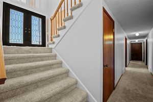 Stairway featuring carpet floors, a textured ceiling, and french doors
