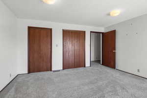 Unfurnished bedroom with two closets, carpet flooring, and a textured ceiling