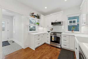 Kitchen with stainless steel appliances, open shelving, white cabinetry, backsplash, quartz countertops. and oak hardwood floors