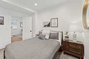 Main floor en-suite bedroom with oak hardwood floors, a desk, and recessed lighting