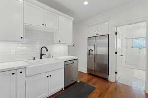 Kitchen with stainless steel appliances, white cabinetry, backsplash, quartz countertops. and oak hardwood floors