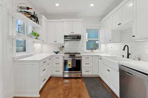 Kitchen with stainless steel appliances, open shelving, white cabinetry, backsplash, quartz countertops. and oak hardwood floors