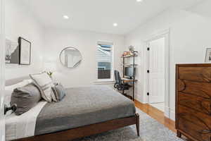 Main floor en-suite bedroom with oak hardwood floors, a desk, and recessed lighting