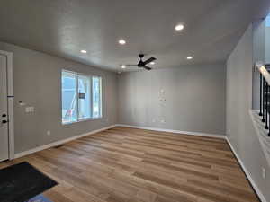 Unfurnished room featuring light wood finished floors, ceiling fan, recessed lighting, and stairs
