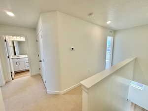 Hallway with light colored carpet, a textured ceiling, and an upstairs landing