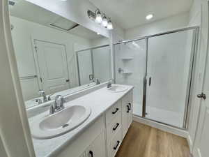 Full bathroom featuring wood finished floors, double vanity, a stall shower, and recessed lighting