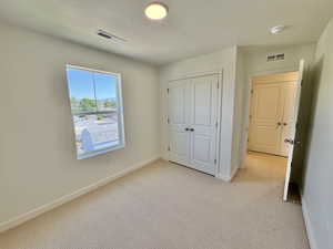 Unfurnished bedroom featuring light colored carpet, a textured ceiling, and a closet