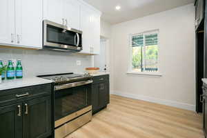 Kitchen with stainless steel appliances, light wood finished floors, backsplash, light countertops, and white cabinets