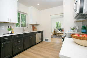 Kitchen with appliances with stainless steel finishes, white cabinetry, light wood-style floors, light countertops, and backsplash