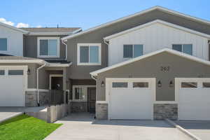 View of front facade featuring concrete driveway, stone siding, and board and batten siding