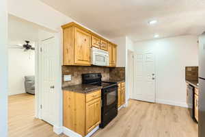 Kitchen featuring black appliances, light wood-style floors, decorative backsplash, dark countertops, and a textured ceiling