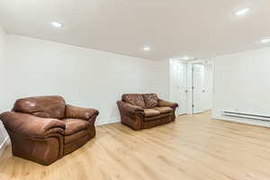 Sitting room with light wood-style floors, baseboard heating, recessed lighting, and a textured ceiling