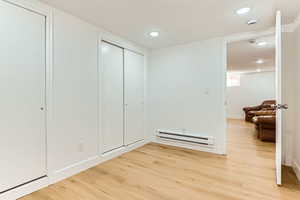 Bedroom featuring a baseboard radiator, light wood finished floors, recessed lighting, and a closet