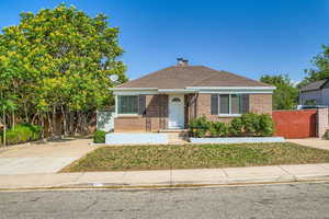 Bungalow-style home featuring brick siding, a chimney, a shingled roof, and concrete driveway