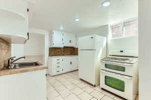 Kitchen featuring white appliances, tasteful backsplash, white cabinets, recessed lighting, and a textured ceiling