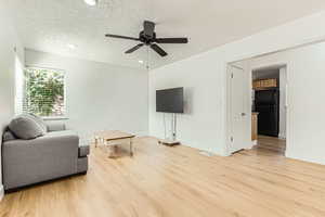 Living room featuring light wood-type flooring, a textured ceiling, a ceiling fan, and recessed lighting