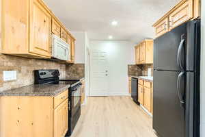 Kitchen featuring black appliances, light brown cabinets, light wood-type flooring, a textured ceiling, and tasteful backsplash