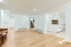 Living area with a baseboard radiator, stairway, light wood-style floors, and recessed lighting