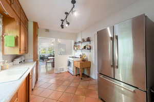 Kitchen with freestanding refrigerator, white gas range oven, light countertops, light tile patterned floors, and a chandelier