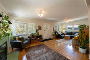 Living area with wood finished floors, a tiled fireplace, crown molding, and ceiling fan