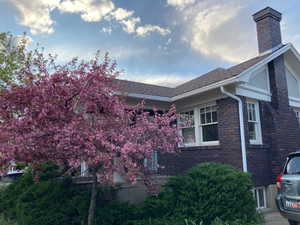 View of side of home with a chimney, a shingled roof, and brick siding