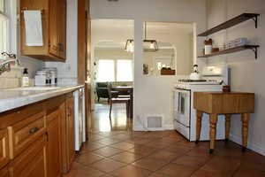 Kitchen featuring white appliances, brown cabinets, light countertops, dark tile patterned flooring, and arched walkways