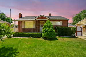 View of front of house featuring brick siding, a chimney, a front yard, and a shed