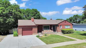 Single story home featuring brick siding, a garage, a chimney, concrete driveway, and a front yard