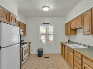 Kitchen with white appliances, light flooring, a textured ceiling, and light countertops