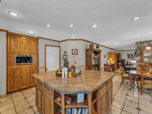 Kitchen with open shelves, stainless steel microwave, ornamental molding, light tile patterned flooring, and brown cabinetry