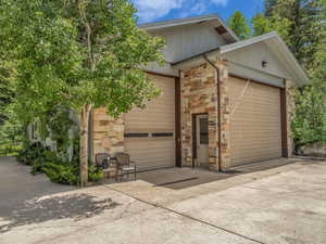 View of side of property with concrete driveway, stone siding, and an attached garage
