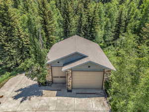View of front of home with roof with shingles, stone siding, a forest view, concrete driveway, and an attached garage