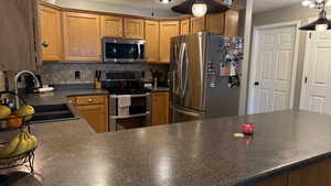 Kitchen featuring appliances with stainless steel finishes, decorative backsplash, dark countertops, and brown cabinets