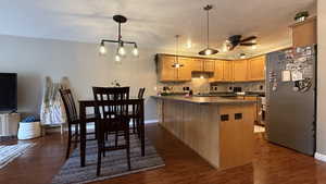 Kitchen with freestanding refrigerator, a peninsula, dark countertops, ceiling fan, and dark wood-style flooring
