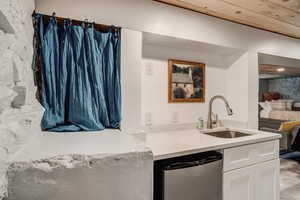 Kitchen featuring stainless steel dishwasher, white cabinetry, and light countertops