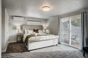 Carpeted bedroom featuring access to exterior, multiple windows, a textured ceiling, and a wall mounted air conditioner