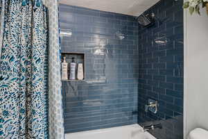 Bathroom featuring a textured ceiling and shower / bath combination with curtain