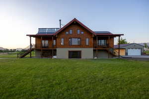 Front of property at dusk with stairs, roof mounted solar panels, a yard, and a detached garage