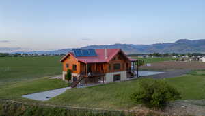 View of front of home with stairway, roof mounted solar panels, a front lawn, and a mountain view