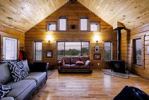 Living area with wooden ceiling, a wood stove, wood finished floors, wooden walls, and high vaulted ceiling