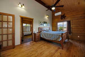 Primary bedroom featuring multiple windows, hardwood finished floors, high vaulted ceiling and wood walls