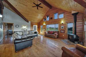 Living room featuring a wood stove, high vaulted ceiling, wood finished floors, ceiling fan, and wooden walls