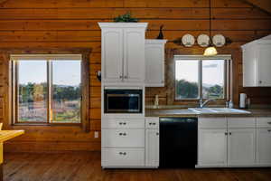 Kitchen featuring black dishwasher, stainless steel microwave, wooden walls, white cabinetry, and hardwood-style floors